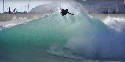 Surfer crouches on a turquoise wave as it curls toward the beach.