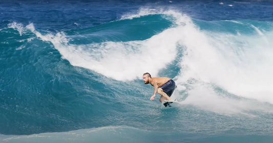 Male surfer with dark shorts rides a turquoise wave on a shortboard.