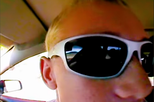 Close-up of a person wearing white wraparound sunglasses in a car.